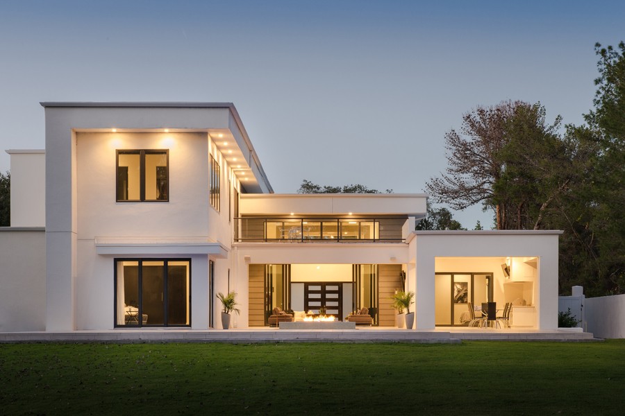 A well-lit home with a well-manicured lawn and fireplace after dark. There are trees in the background, and the house is a modern style.