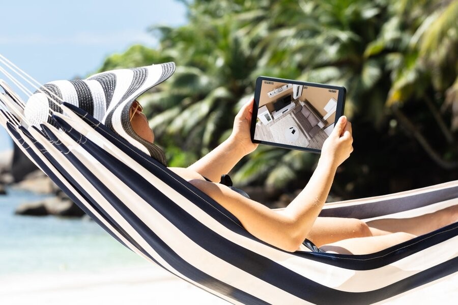 A woman on vacation on the beach checking on on her home via a monitored security system.